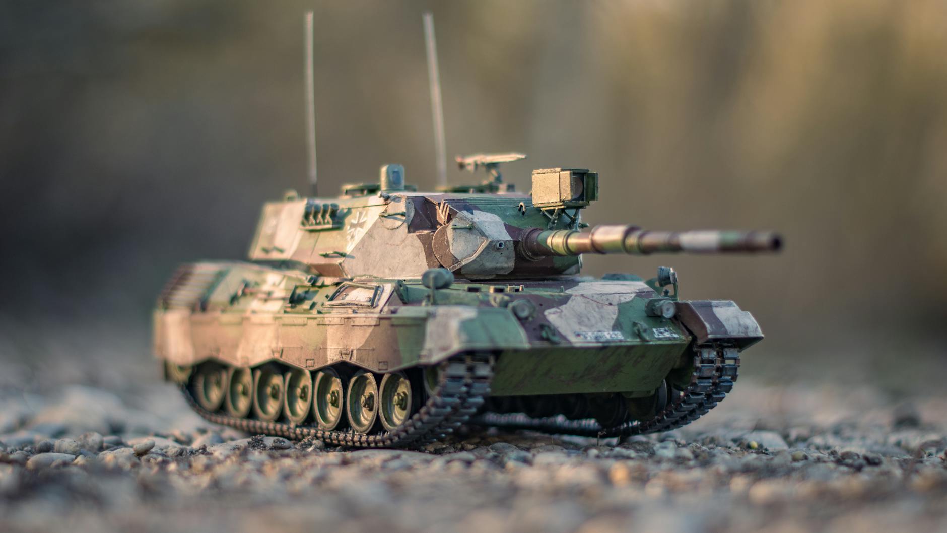 Detailed view of a camouflage military tank model on gravel road outdoors.