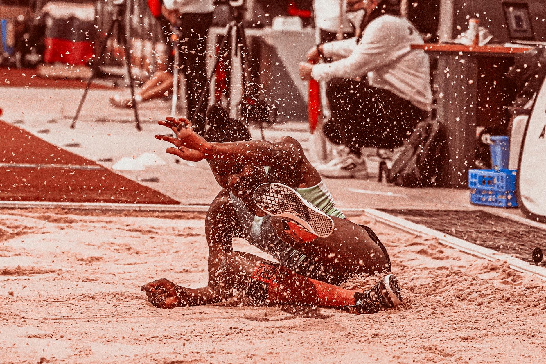 Athlete landing in sand during a long jump competition, showcasing athleticism and motion.